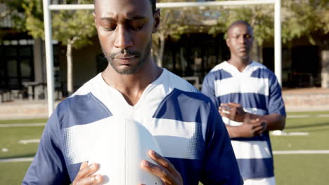holding rugby ball, african american male athlete focusing before game with teammate, on field