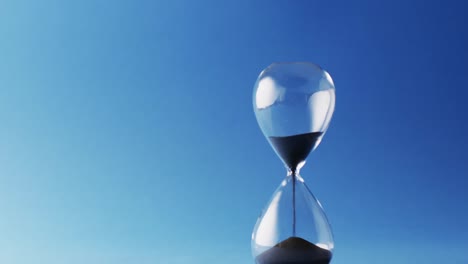 video of hourglass with black sand pouring with copy space on blue background