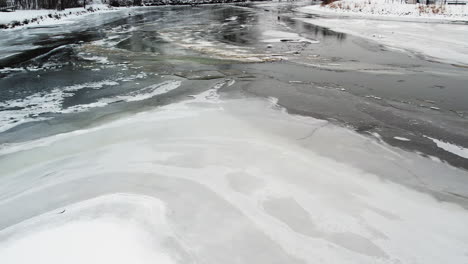 Drohnen-Auslegerschuss-über-Eisdecke-Auf-Teich-Zu-Mit-Schmutz-Und-Ablagerungen-Gefülltem-Fluss