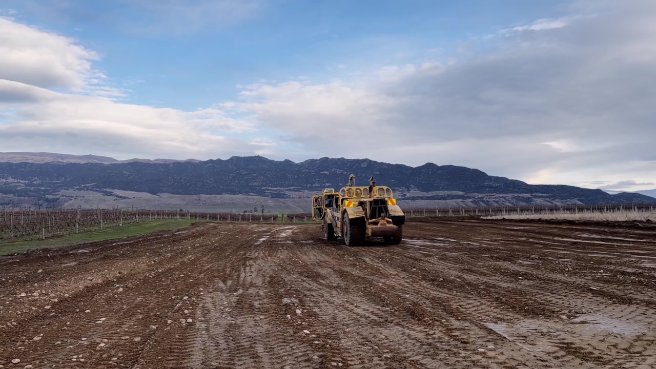 Uno scraper gommato trasporta terra in un sito agricolo, preparando il terreno per il futuro sviluppo di un vigneto a Central Otago, Nuova Zelanda