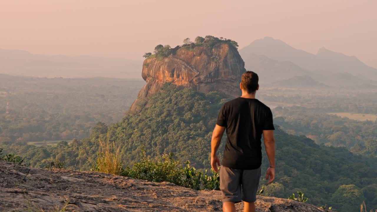 A contemplative moment as a man gazes toward the iconic Sigiriya Rock fortress in Sri Lanka during the golden light of sunrise.
