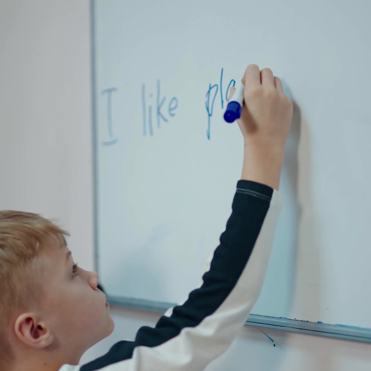 Little boy near the blackboard. Schoolboy standing near the white board and writing sentences with a marker. Elementary school. Back to school.