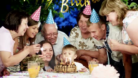 little boy in cone hat blowing candles on birthday cake