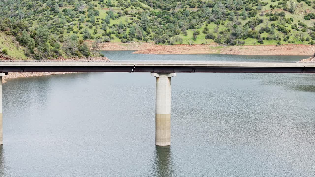 A close up aerial shot of a car driving across the Don Pedro Reservoir Bridge, showcasing the contrast between road and water. Shot on a DJI Air 3S.