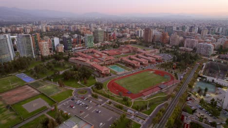 Las-condes-Neighborhood-Santiago-de-Chile-Cityscape-at-sunset,-drone-aerial-orbit-around-Military-School-Bernardo-O'Higgins-high-urban-buildings