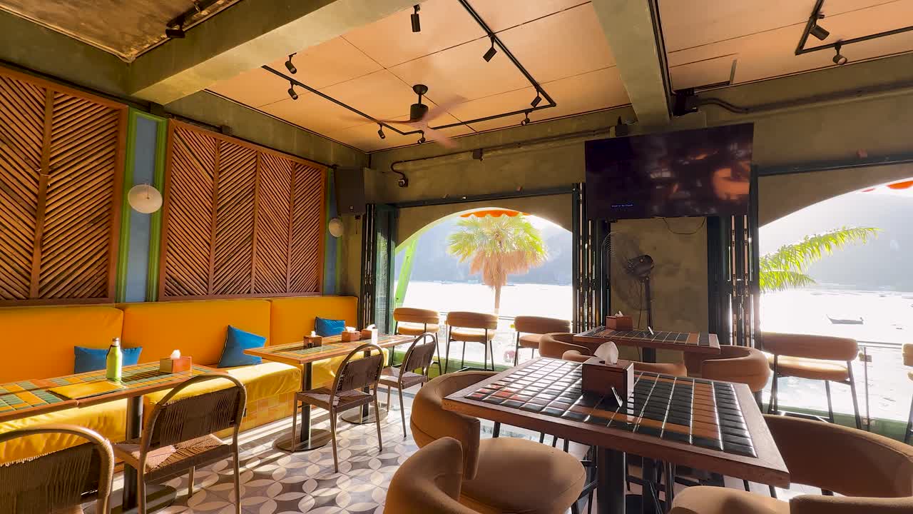 Ampia inquadratura fissa di un interno vibrante e vuoto di un ristorante tropicale che si affaccia su una spiaggia soleggiata