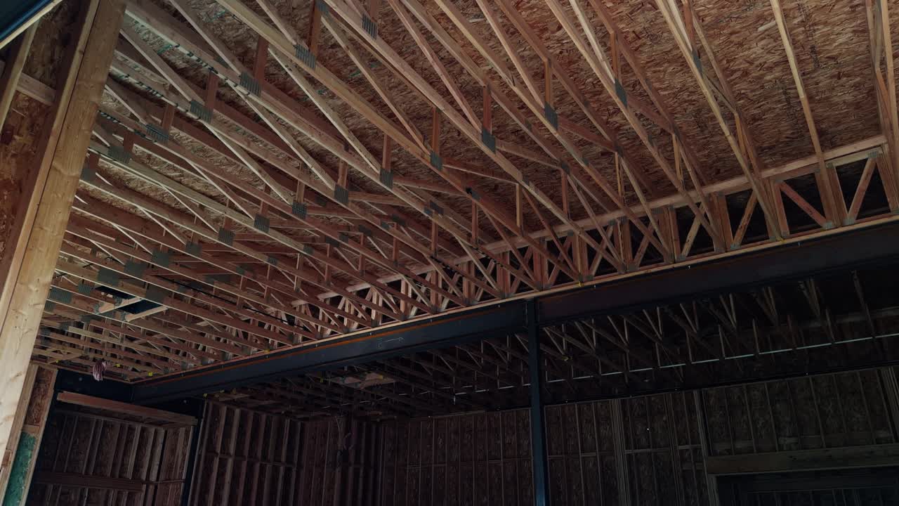 Slow steady pan of exposed wooden roof trusses and central steel beam inside unfinished structure