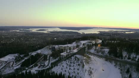 Empuje-De-Drones-De-La-Ciudad-De-Oslo,-Parque-De-Invierno-Parque-De-Invierno-Tryvann-Pasado-Salto-De-Esquí-Al-Atardecer-Holmenkollen-Con-Esquí-De-Fondo-Nórdico