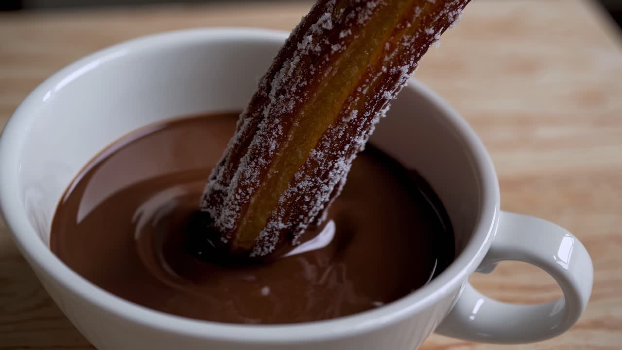 Gros plan vidéo de churros saupoudrés de sucre glace sur une assiette blanche, accompagnés d'une tasse.