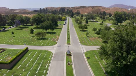 Toma-Aérea-Baja-Volando-Sobre-La-Carretera-Principal-De-Una-Morgue-De-California-Mientras-Un-Desfile-De-Autos-Se-Alinea-Para-Un-Funeral