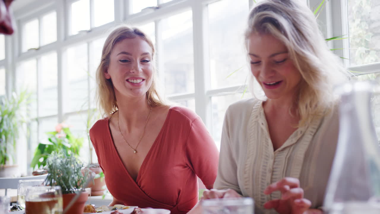 Two young adult white women eating lunch with friends at a restaurant, low angle