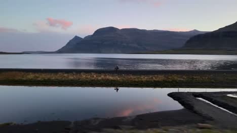 aerial spiral away from bicycle on reflective iceland lake with mountains