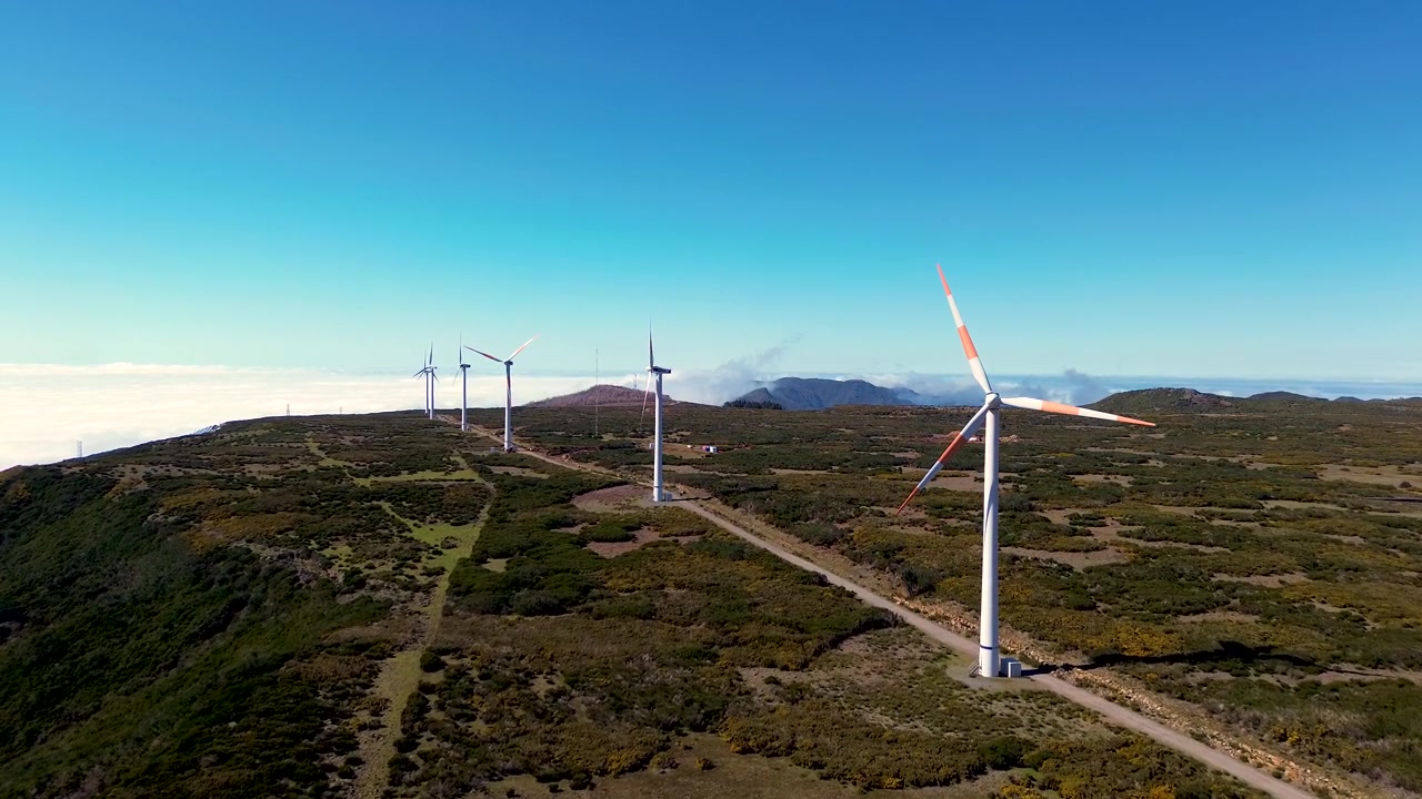 Panorâmica aérea de drone sobre turbinas eólicas no planalto da Paul da Serra, na Madeira, Portugal, com colinas ondulantes e um mar de nuvens ao fundo