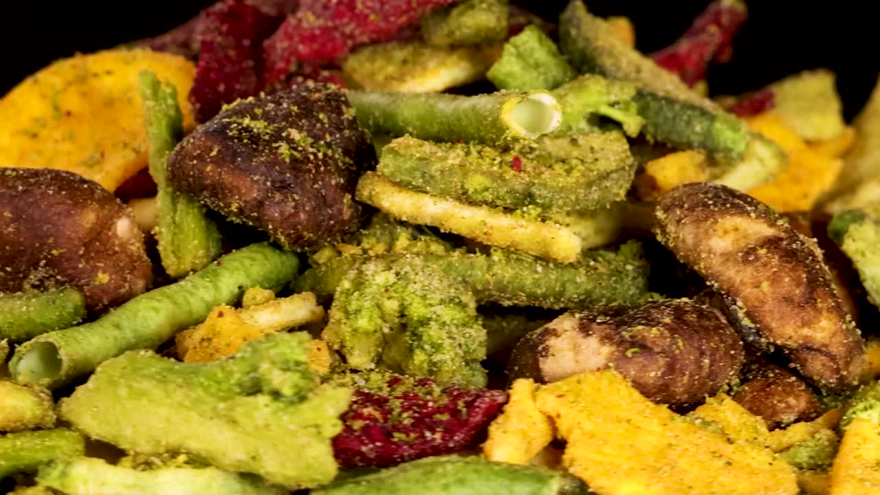 Vista macro di un assortimento di chips di verdure essiccate che ruotano lentamente su uno sfondo scuro