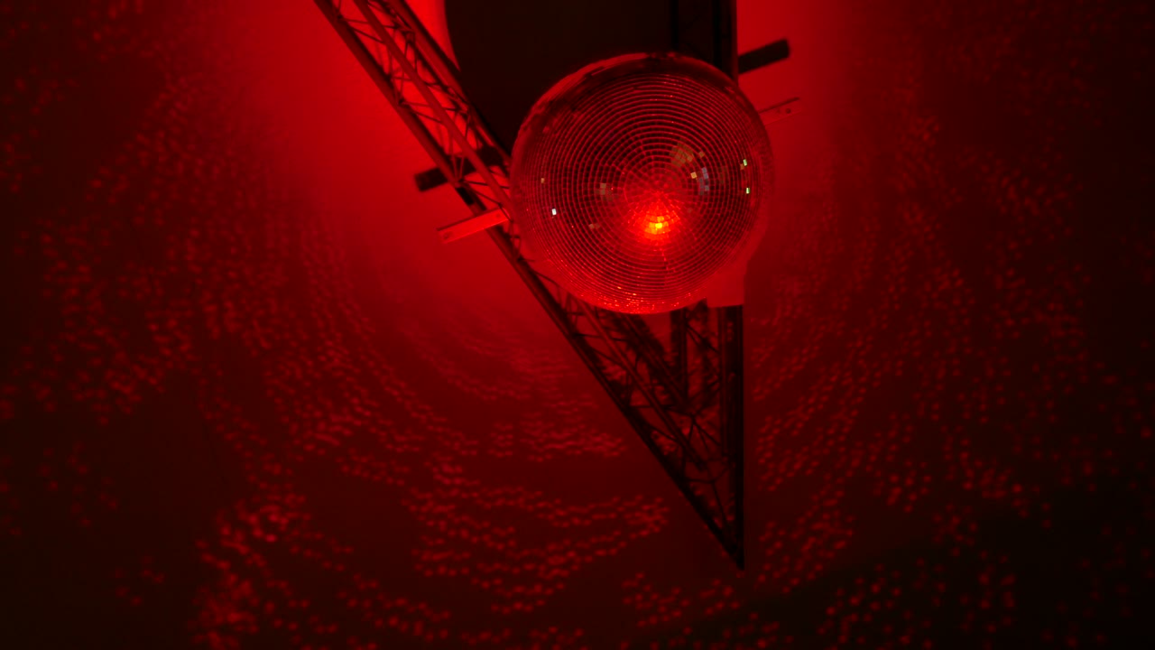 지붕에 있는 다채로운 불빛에 의해 반사되는 회전하는 거울 구 디스코 공의 영상입니다.