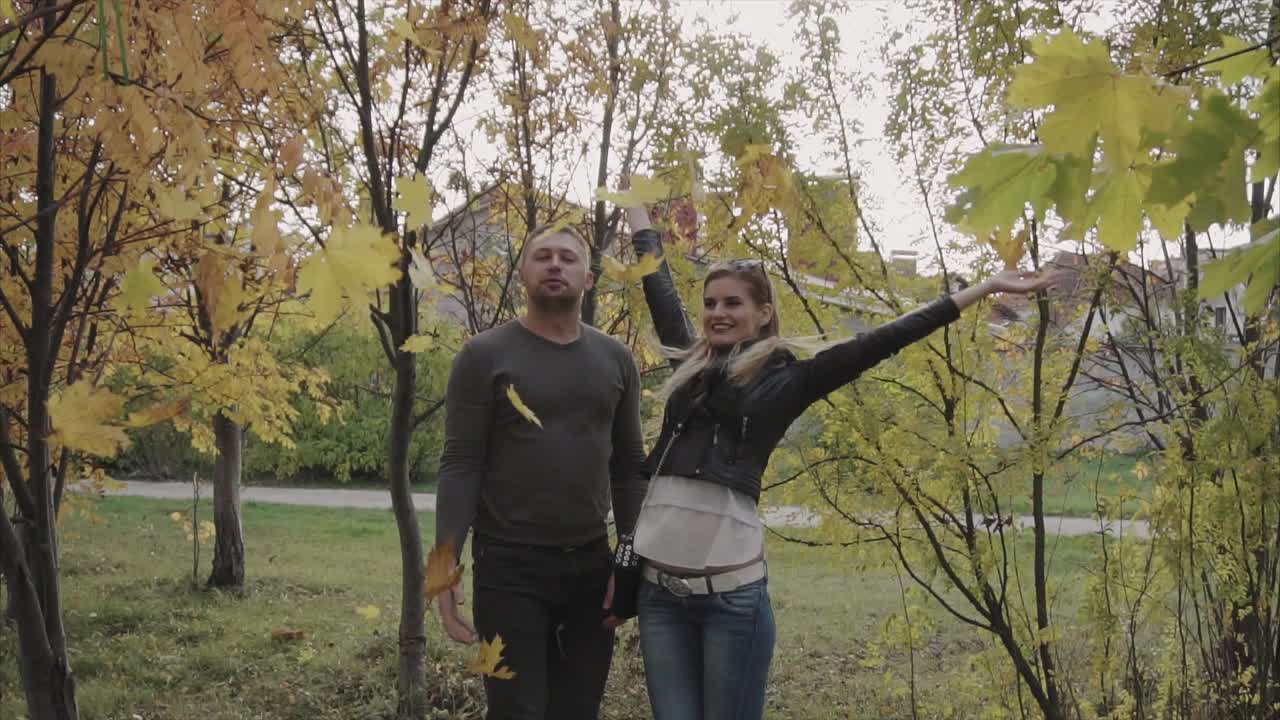 una pareja jugando con hojas de otoño en un parque