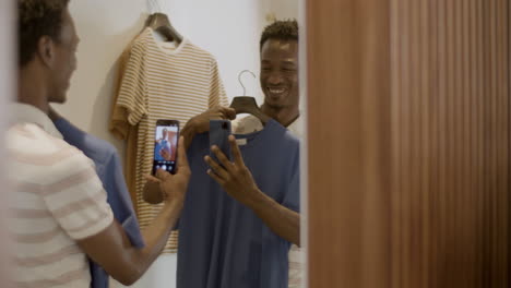 un chico negro feliz tomando una selfie en el camerino de la tienda.