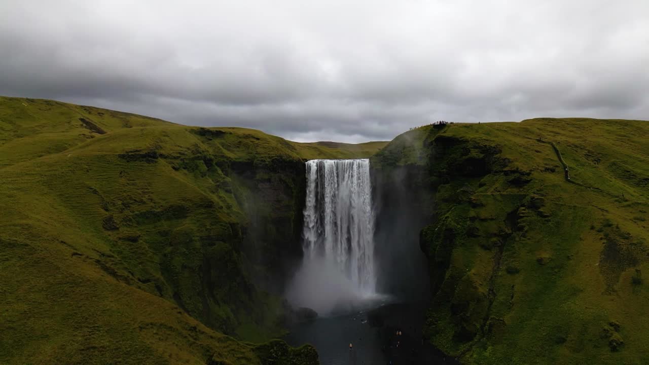 4K cinematic drone footage of Skógafoss Waterfall in Iceland, capturing the immense curtain of water cascading from towering cliffs surrounded by lush green landscapes. Iceland_28
