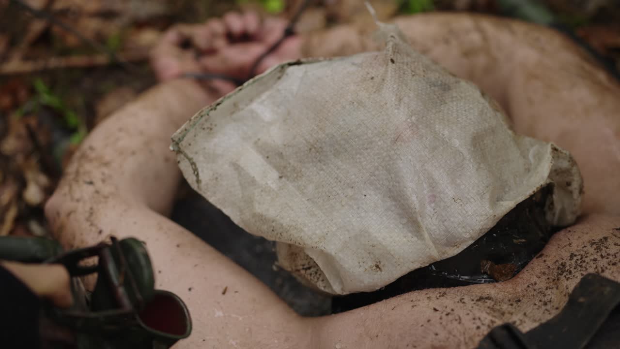 Waterboarding interrogation with hooded, restrained man on forest ground