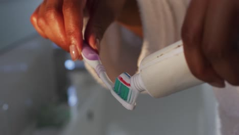 close up of african american woman putting toothpaste on her brush in the bathroom