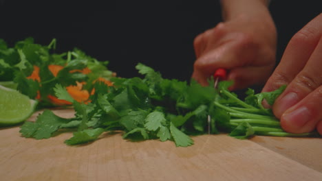 manos de mujer cortando cilantro en una tabla de cortar de madera