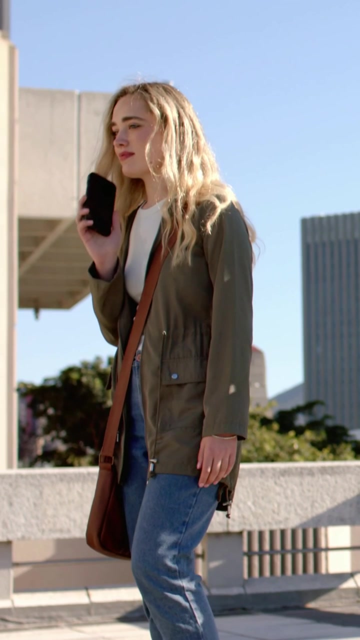 Vertical video: Taking call, woman in anorak gesturing, checking phone for text on plaza, with bag