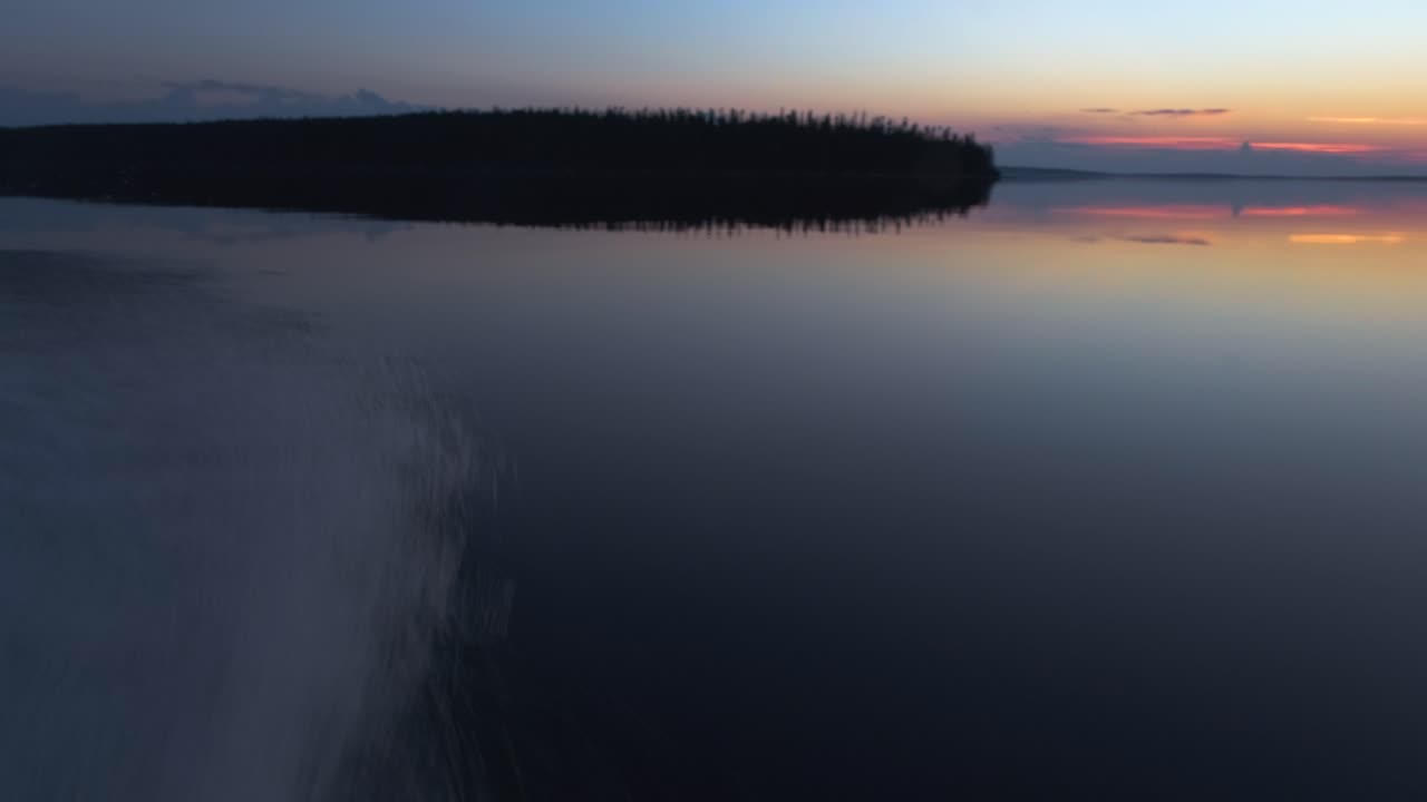 Kameran panorointi, alkaen nopeasti ajavan veneen kyljestä vedenpinnalla ja päättyen kauniiseen, värikkääseen auringonlaskuun järvellä.