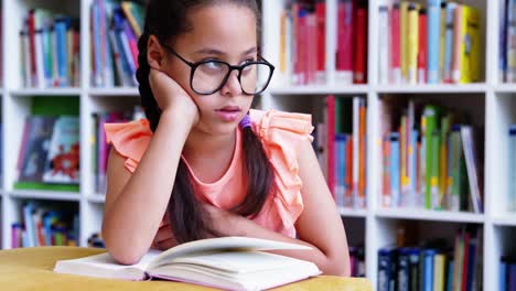 escolar pensativa sentada en la mesa en la biblioteca de la escuela