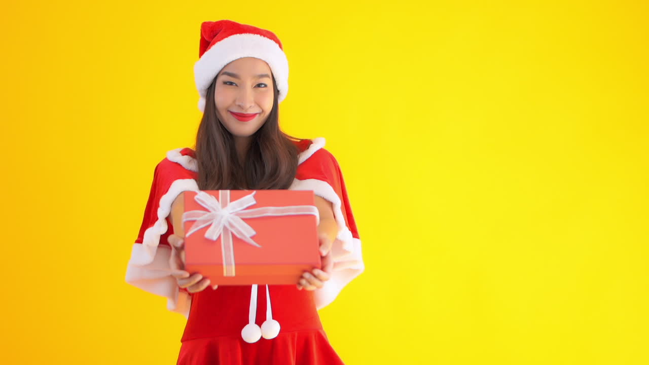 An attractive young Asian woman dressed in a red Santa helper's suit holds a present in her hands. Copy space