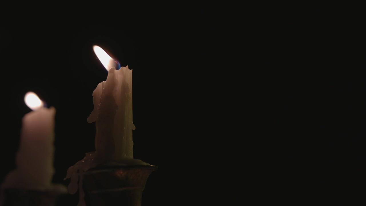 Primo piano di due candele bianche accese su un candelabro che vengono spente dal vento al rallentatore.