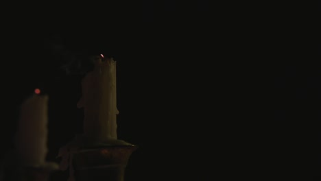 a close up of two white candles lit on a candelabra and being blown out by the wind in slow motion