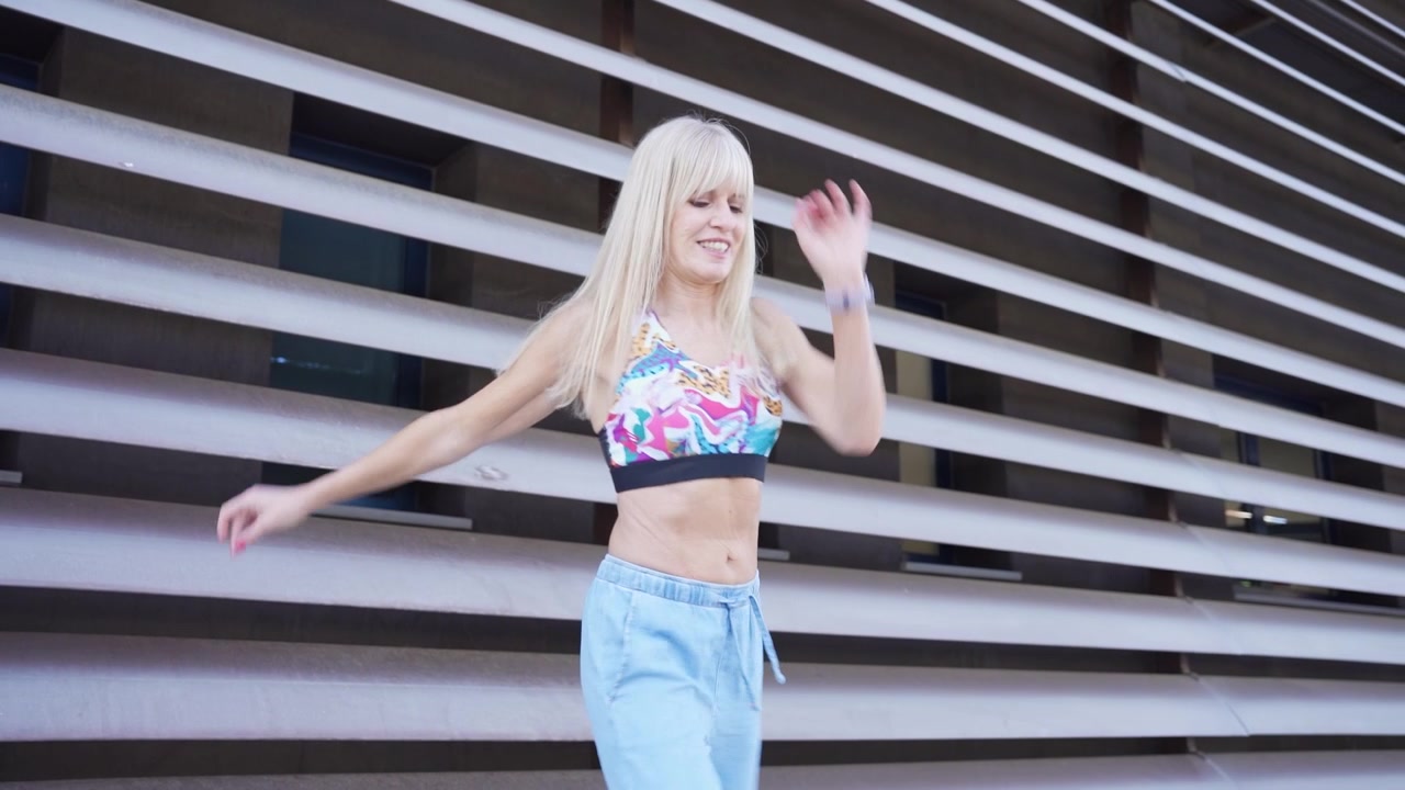 En glad og ubekymret kvinde danser energisk udendørs i trendy sommertøj.