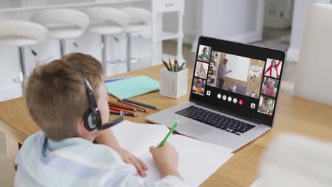 schoolboy using laptop for online lesson at home, with diverse teacher and class on screen