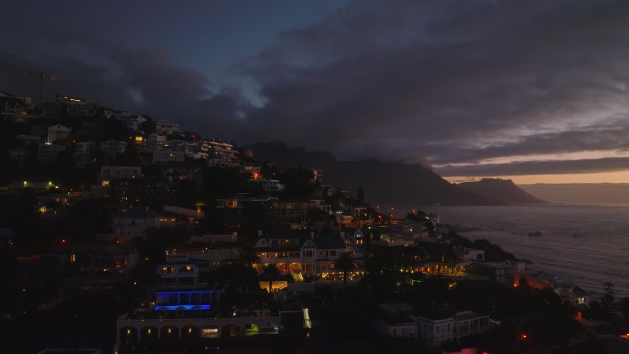 residenze e appartamenti di lusso in pendenza sopra l'acqua. forwards volano sopra la costa del mare in città al crepuscolo. cape town, sudafrica