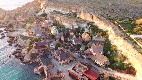 rocky cliff side coastal wooden town in malta island, aerial view during golden sunset