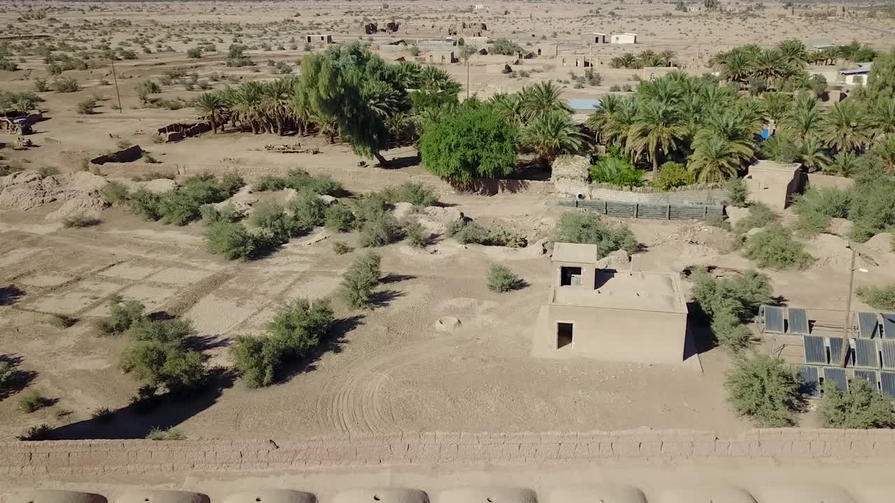 Una fortezza nel deserto situata accanto a un'oasi con torre, palma, dune di sabbia e case di mattoni di fango.