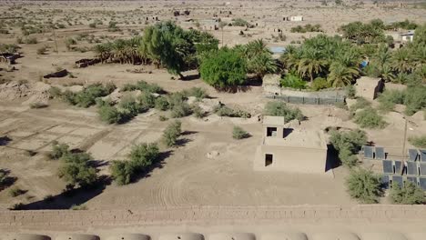 una fortaleza en el desierto ubicada junto a un oasis con torres, palmeras, dunas de arena y casas de adobe