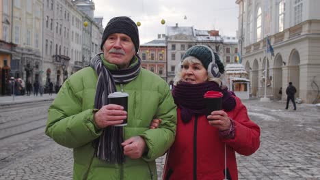 Senior-wife-husband-tourists-drinking-from-cups,-enjoying-hot-drink-tea-on-city-central-street