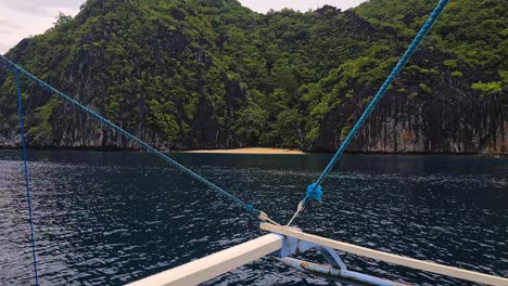 filipino bangka catamaran boat sailing by hidden beach under limestone cliffs on uninhabited island, passenger pov