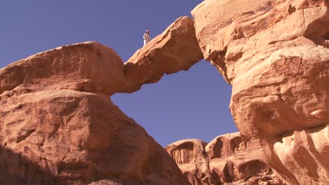 an amazing arch formation in the sadi desert in wadi rum jordan with a bedouin man walking through