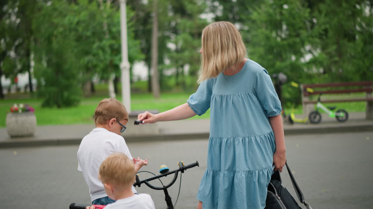 엄마는 어린 아들의 머리를 조심스럽게 고, 아들은 안경을 쓰고 자전거에 앉아서 손으로 머리를 조정합니다.
