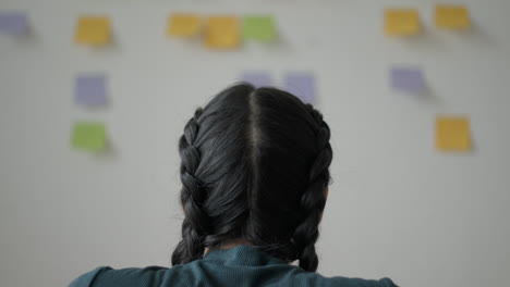 a woman is studying a whiteboard filled with post-it notes