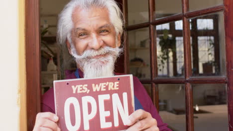 happy senior biracial business owner with long beard holding shop sign and smiling slow motion