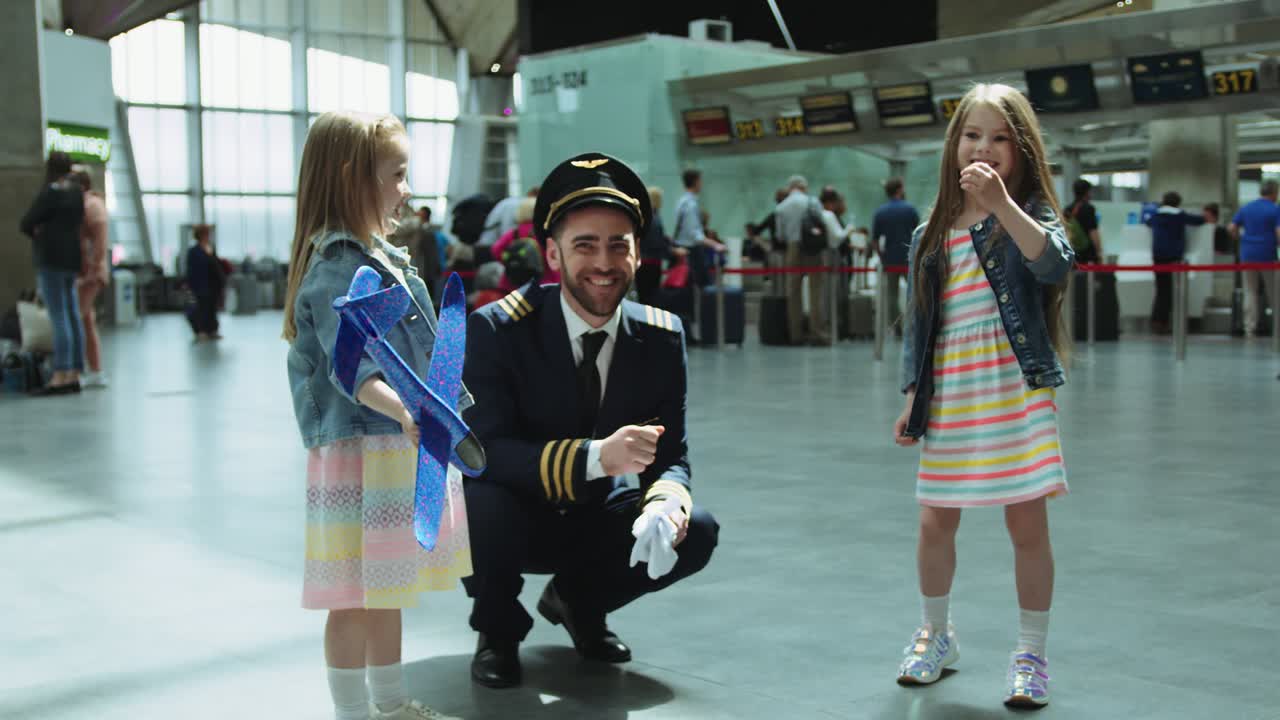 기쁜 어린 소녀들이 공항 터미널에서 다디스 조종사 모자를 입으려고 노력하며 행복하고 웃고 있습니다. 빨간 카메라에서 촬영된 영화입니다.