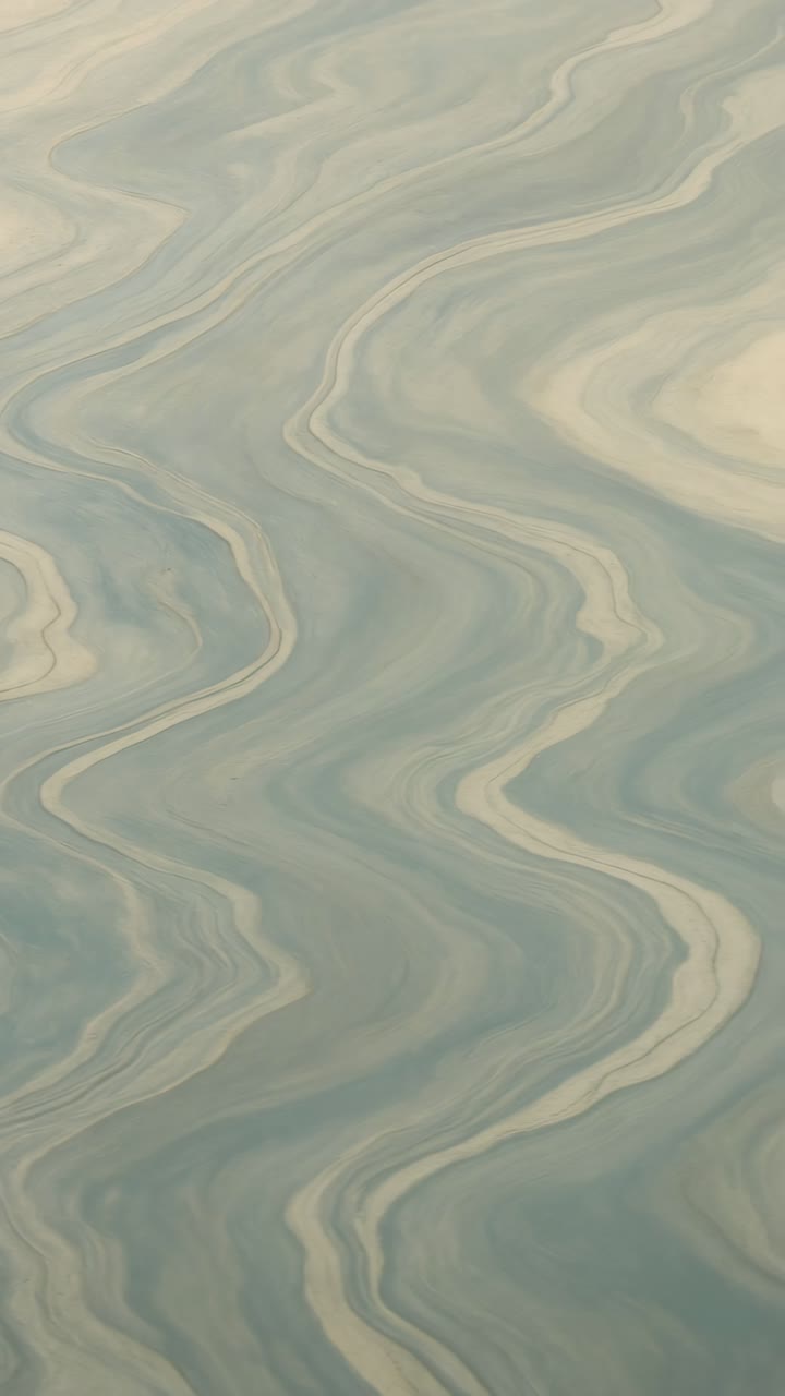 Top-down video shot of a marble-like pattern with flowing blue and beige swirls