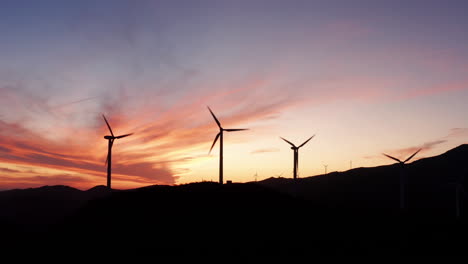 long line of beautiful windmill turbines harnessing clean, green, wind energy rise above the landscape in this breathtaking silhouette scene