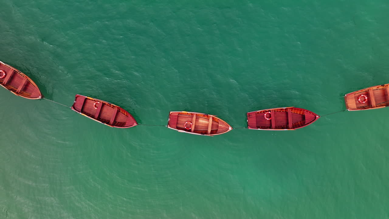 Top down drone shot of wooden rowing boats at famous Lago di Braies, a popular tourist destination in the Italian Alps