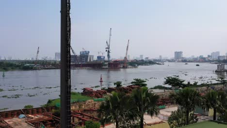 ascending aerial shot of ultra modern mobile phone tower disguised as a palm tree against a background of a riverfront construction site with city buildings, cranes and boat traffic on the river