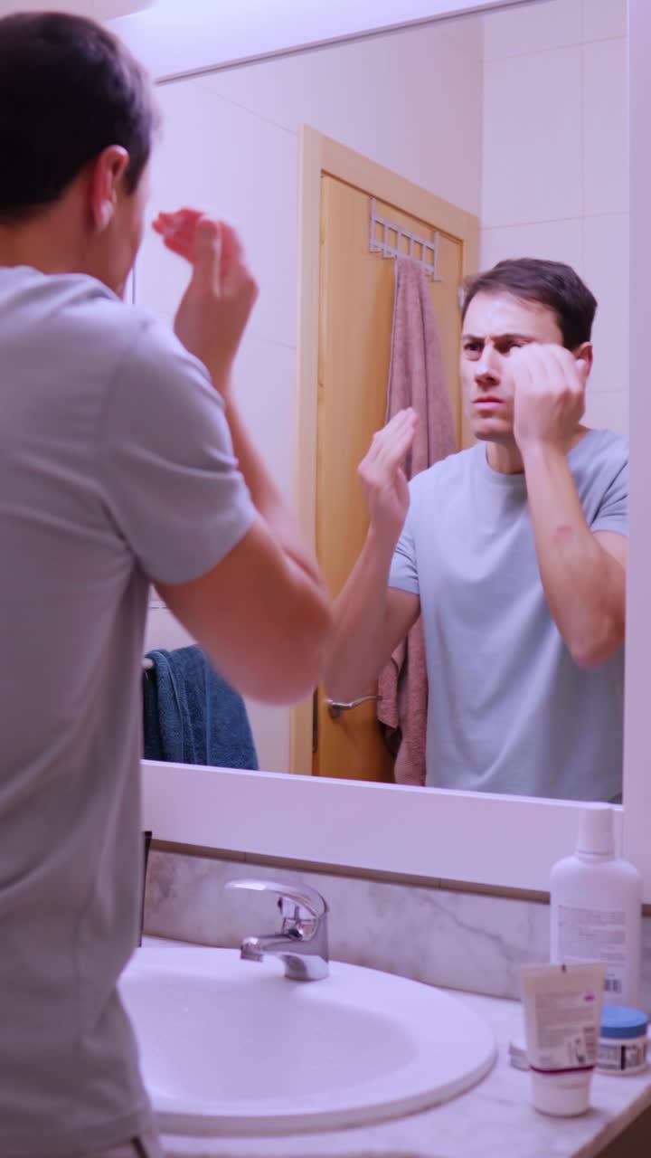 Man applying face cream in bathroom mirror