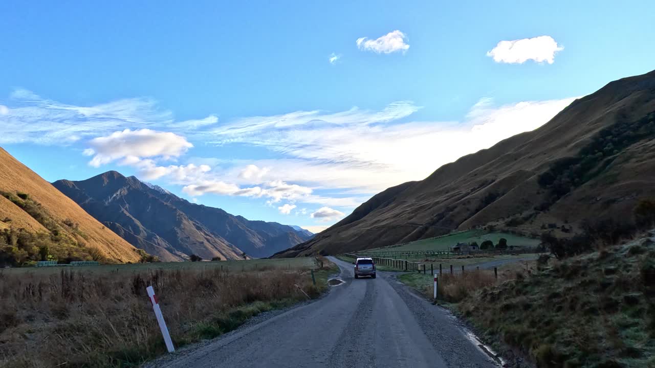 Veicolo percorre una strada sterrata in una valle montana all'alba, telecamera fissa in avanti, vista ampia
